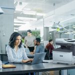 Imprimante multifonction couleur Xerox® C325 dans une situation de bureau Femme professionnelle tapant sur un ordinateur portable au bureau dans un environnement de bureau à côté d'une imprimante Xerox® C325
