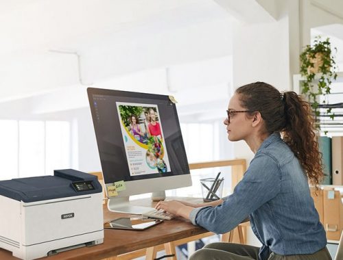 Une femme assise à un bureau, concentrée sur son travail, avec une imprimante Xerox® C320 couleur
