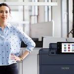 Une femme se tenant à côté de l'imprimante Xerox® PrimeLink® Série C9200 dans un environnement de bureau moderne Une femme se tenant à côté de l'imprimante Xerox® PrimeLink® Série C9200 dans un environnement de bureau moderne